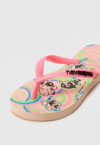 Rosa flip-flop med en texturerad rem, ett mönstrat fotutrymme med serietidningskaraktärer och en solid, lätt sula.