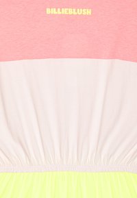 Rosa och ljusbeige bomullstopp med rynkad nederkant, som har en neon-grön underdel och "BILLIEBLUSH" logotyp i gult.