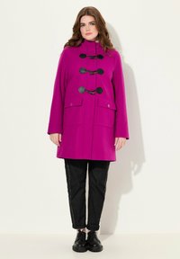 Fuchsia frakke med høj krave, toggle-lukning og to forlommer. Stilet med sorte bukser og sko. Glat tekstur.