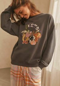 Gray oversized sweatshirt with colorful floral and pumpkin graphic, paired with plaid pajama pants in orange, cream, and light blue tones.