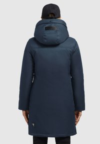 Marineblaue isolierte Parka mit großer Kapuze, strukturiertem Stoff und einem Logopatch auf dem Rücken. Verfügt über seitliche Taschen und eine Länge bis zur Mitte des Oberschenkels.