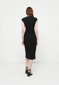 Rochie neagră, ajustată, cu mâneci tip capac, lungime până la genunchi și talie definită. Model îmbrăcat cu sandale negre cu toc înalt și curea. Fundal simplu.