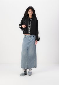 Veste noire cropped avec des manches rayées, top rayé en dessous, jupe maxi en denim bleu clair, chaussures à plateforme grises et sac à main noir.