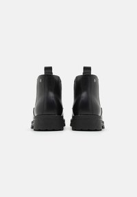 Bottines noires avec une finition en cuir lisse, des coutures renforcées, des languettes de traction et une semelle en caoutchouc texturé pour une adhérence et une durabilité accrues.