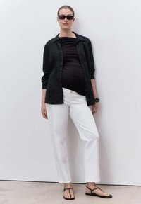Camicia nera con bottoni, top nero aderente, pantaloni bianchi a gamba dritta e sandali neri piatti. Design minimalista con una texture liscia.