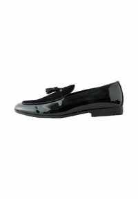 Schwarzer Lacklederschuh mit einem Wildlederakzent. Ausgestattet mit einer flachen Sohle und einem abgerundeten Zehendesign, verziert mit einer kleinen dekorativen Quaste.