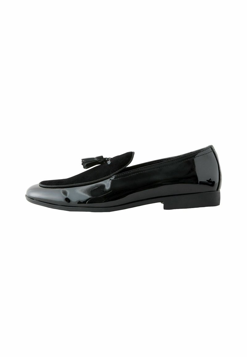 Black patent leather loafer with a suede accent. Features a flat sole and a rounded toe design, embellished with a small decorative tassel.
