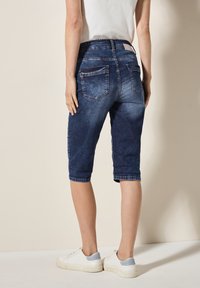 Shorts en denim bleu foncé, avec une taille mi-haute, un ourlet retroussé et deux poches arrière. Stylés avec une texture lisse et une décoloration subtile.