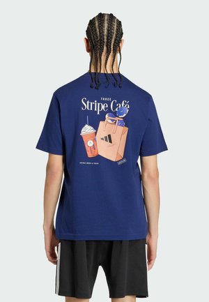 Person mit geflochtenen Haaren, die ein blaues T-Shirt mit einem Kaffeegetränk, einer Einkaufstasche und dem Schriftzug „Three Stripe Café“ auf dem Rücken trägt, kombiniert mit schwarzen Shorts.