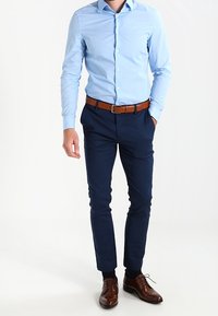 Ljusa blå, långärmad skjorta kombinerad med mörkblå byxor, accentuerad med ett brunt bälte och bruna dressade skor, vilket framhäver en stilren passform.