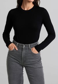 Top nero a manica lunga con scollo rotondo, abbinato a jeans grigi a vita alta con tasche frontali e chiusura con bottoni.