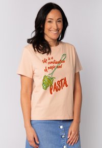Perzikkleurig katoenen T-shirt met een afbeelding van pasta op een vork. De tekst luidt "het leven is een combinatie van magie en PASTA" in rood en groen.