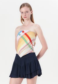 Top multicolore sans bretelles avec des rayures diagonales jaunes, roses, vertes et rouges. Assorti à une jupe à volants en tulle bleu marine.