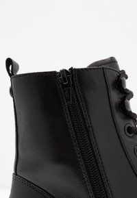 Botín de cuero negro hasta el tobillo con cremallera lateral, cordones redondos y textura suave. Incluye tres ojetes negros y una lengüeta.