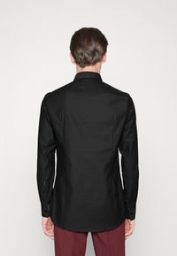 Czarna koszula z długim rękawem, z usztywnionym kołnierzem i zapinanymi na guziki mankietami, o gładkiej fakturze i dopasowanym kroju. Widok od tyłu.