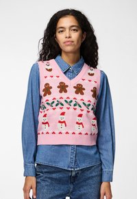 Chaleco de punto rosa con un diseño festivo que incluye hombres de jengibre, muñecos de nieve y detalles de acebo, superpuesto a una camisa de mezclilla azul.