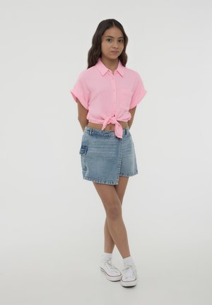 Camisetta rosa corta con maniche corte, annodata in vita; gonna di jeans con tasca laterale; sneaker bianche con dettagli rossi.