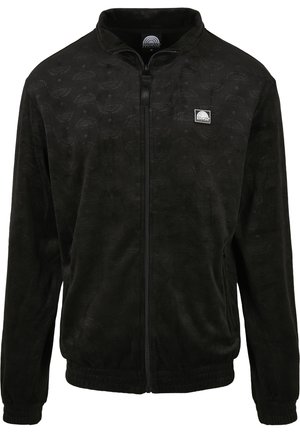 Chaqueta de forro polar negra con cierre de cremallera, que presenta un patrón texturizado, cuello alto y puños acanalados. Parche de logo en el lado izquierdo del pecho.