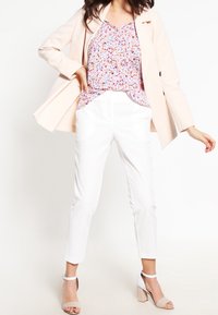 Blush pink blazer over en blomstret top, parret med hvide tapered bukser og nude ankelremssandaler. Glat stof, moderne design.