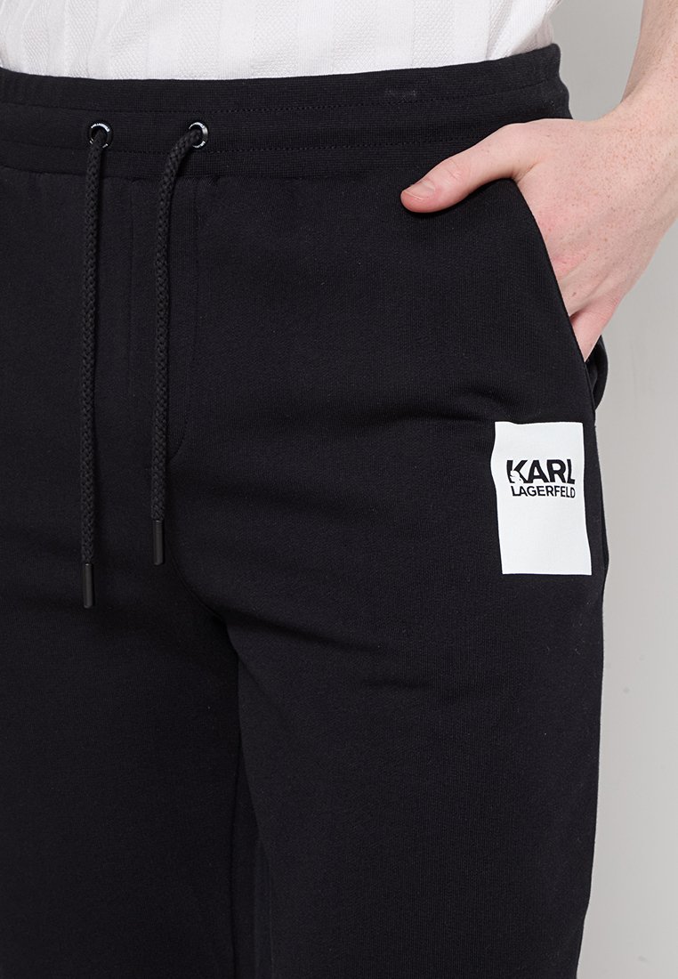 Pantaloni jogger neri in cotone con vita elasticizzata, dotati di cordoncini regolabili e di un'etichetta bianca con logo sulla coscia.