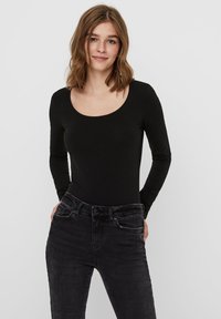 Fekete, hosszú ujjú body, mély dekoltázsú, sima anyagból, sötét szürke, szűk farmerral viselve, bemutatva egy laza megjelenést.