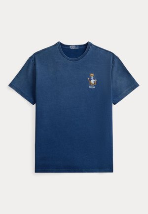 Granatowy t-shirt z krótkim rękawem i okrągłym dekoltem, z małym wyszywanym misiem w kurtce siedzącym na krześle ponad napisem „POLO” na klatce piersiowej.