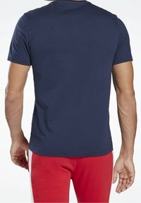 Granatowa bawełniana koszulka z krótkim rękawem, okrągłym dekoltem i gładką fakturą. Nosi się z czerwonymi spodniami z białymi paskami po bokach.