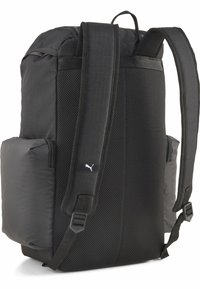Zaino nero con schienale in rete imbottita, spallacci regolabili, doppie tasche laterali e una piccola etichetta con logo. Presenta un materiale esterno morbido e una forma strutturata.