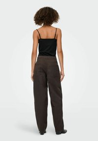 Top noir à bretelles fines associé à un pantalon large décontracté marron foncé doté de deux poches arrière et d'une texture lisse.