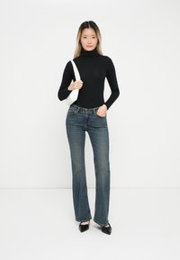 Svart høyhalset topp, blå denim flared jeans, sorte spisse sko, hvit håndveske med stropp. En enkel, tettsittende design.