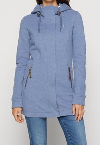 Giacca con cappuccio blu in morbido tessuto, con chiusura a zip frontale, tasche laterali con zip e coulisse regolabile sul cappuccio.
