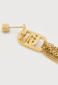 Náušnice so zlatým tónom, s prepojeným reťazcom a viacerými visiacími zlatými reťazcami, na bielom pozadí.