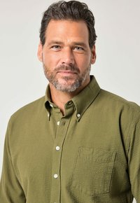 Olivgrünes Hemd mit Knopfleiste aus strukturiertem Stoff, mit einer Brusttasche und weißen Knöpfen. Es hat einen klassischen Kragen und eine legere Passform.