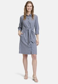 Abito a strisce in blu navy e bianco, con bottoni sul davanti, cinture in vita, maniche lunghe e tasche laterali. Tessuto di cotone morbido.