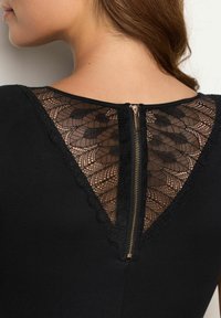 Black garment with a lace yoke featuring a scalloped edge, central zipper fastener, and intricate floral lace pattern on the back.