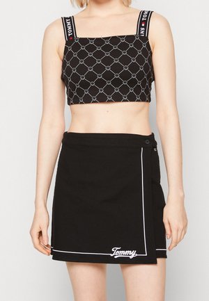 Czarny krótki top z białym geometrycznym wzorem i oznakowanymi paskami; czarna spódnica kopertowa z białym akcentem szwów i logo na dole.