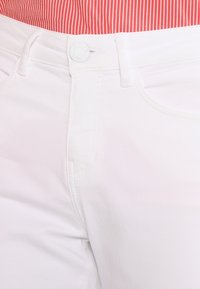 White cotton pants feature a slim fit, front pockets, and a smooth texture. A white button fastens the waist.