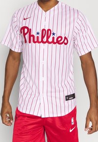 Biała koszulka baseballowa z czerwonymi prążkami, logo "Phillies" w czerwonych literach, zapięcie na guziki, krótkie rękawy. Noszona z czerwonymi szortami.