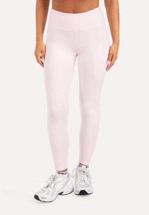 Kvinde iført lyserøde højttaljede leggings og hvide sportssko med hvide sokker på ensfarvet baggrund.