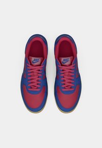 Nike sneakers har et blåt og rødt farveskema, tekstiloverdel, rund tå og flade snørebånd. Sålen er i farven gummi, hvilket tilføjer kontrast.