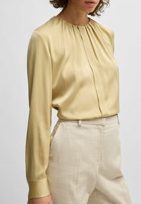 Zijde blouse in een lichtgele kleur met een ronde halslijn, geplooide voorkant en lange mouwen, gecombineerd met lichtbeige broeken.