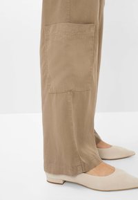 Beige wijde broek met een zijzak; zachte stof met een gladde textuur. Gecombineerd met lichtgekleurde platte schoenen met een spitse neus.