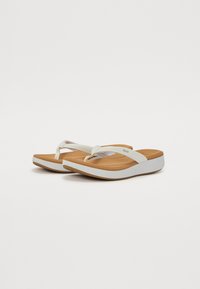 White flip-flops with a textured brown footbed, featuring a curved white sole and minimalist straps. Reinforced toe post for support.
