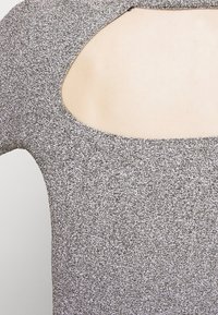 Silver textured fabric top with a wide cut-out at the back. The material is slightly sparkling, enhancing its visual appeal.