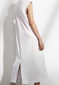 Weißes ärmelloses Kleid aus glattem Stoff, mit einem hohen Kragen, seitlichen Schlitzen und einem geraden Schnitt, der unter dem Knie endet.