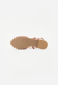 Gewebte Sandalen mit pinkem Riemen und einer strukturierten Gummisohle mit einem hellbraunen Finish. Die Sohle hat geprägte Markendetails. Offenes Rückendesign.