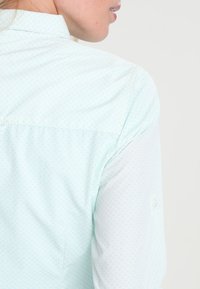 Camicia azzurra chiara con piccolo motivo a pois, con colletto a bottone e polsini. Realizzata in morbido e leggero tessuto di cotone.