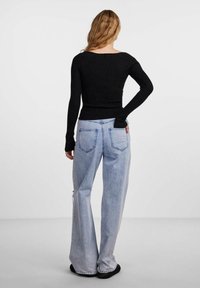 Maglietta nera a coste con maniche lunghe e scollatura a barchetta, abbinata a jeans ampi di colore blu chiaro con tasche posteriori e una vestibilità rilassata.