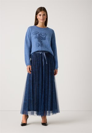 Hellblauer Pullover mit floralem Stickereien, kombiniert mit einem dunkelblauen, gemusterten Tüllrock mit Falten und einem gebundenen Taillenbund. Schwarze Schuhe.
