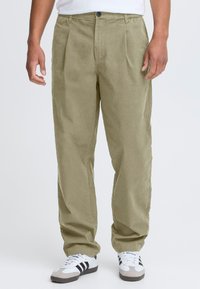 Beige, plissierte Hose aus leichtem Stoff mit entspannter Passform, seitlichen Taschen und Knopfverschluss am Bund.